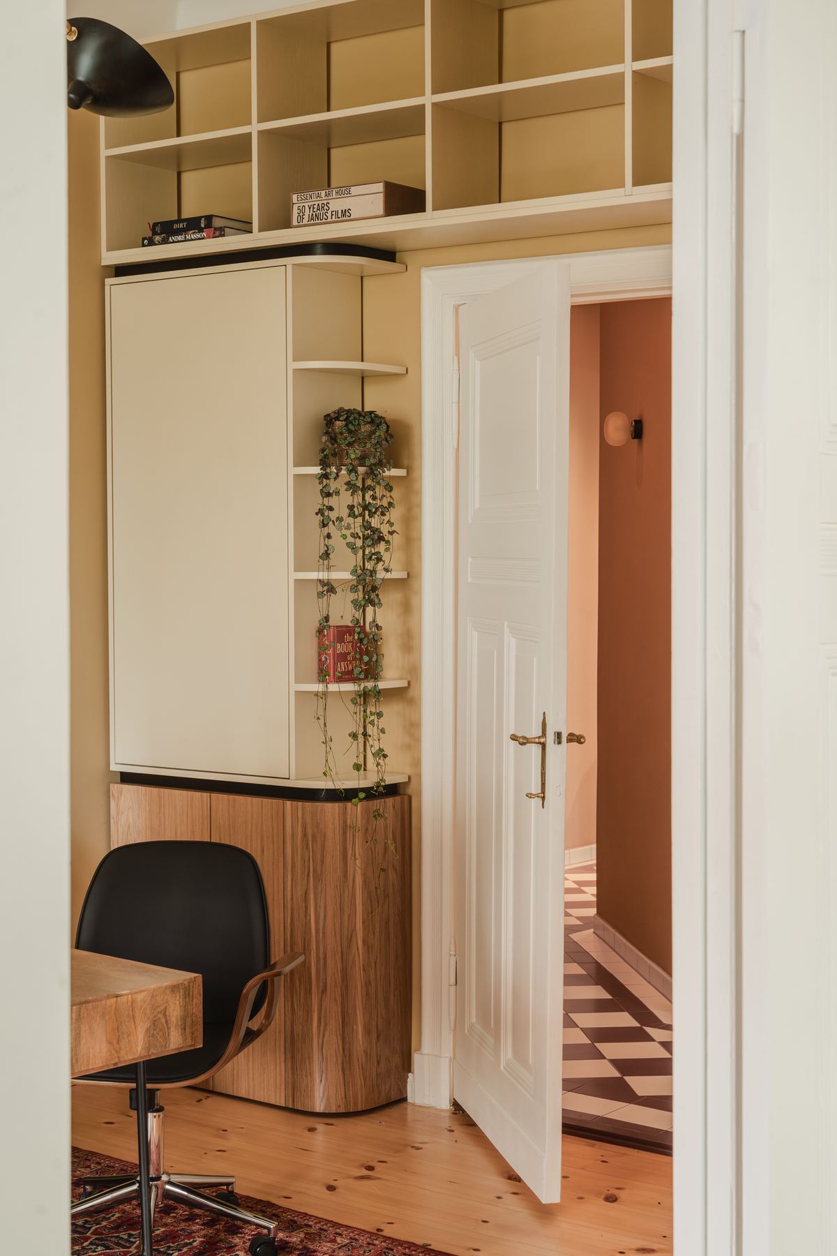 A built-in wooden desk in an alcove with open shelving above it and a black task chair pulled up to it.