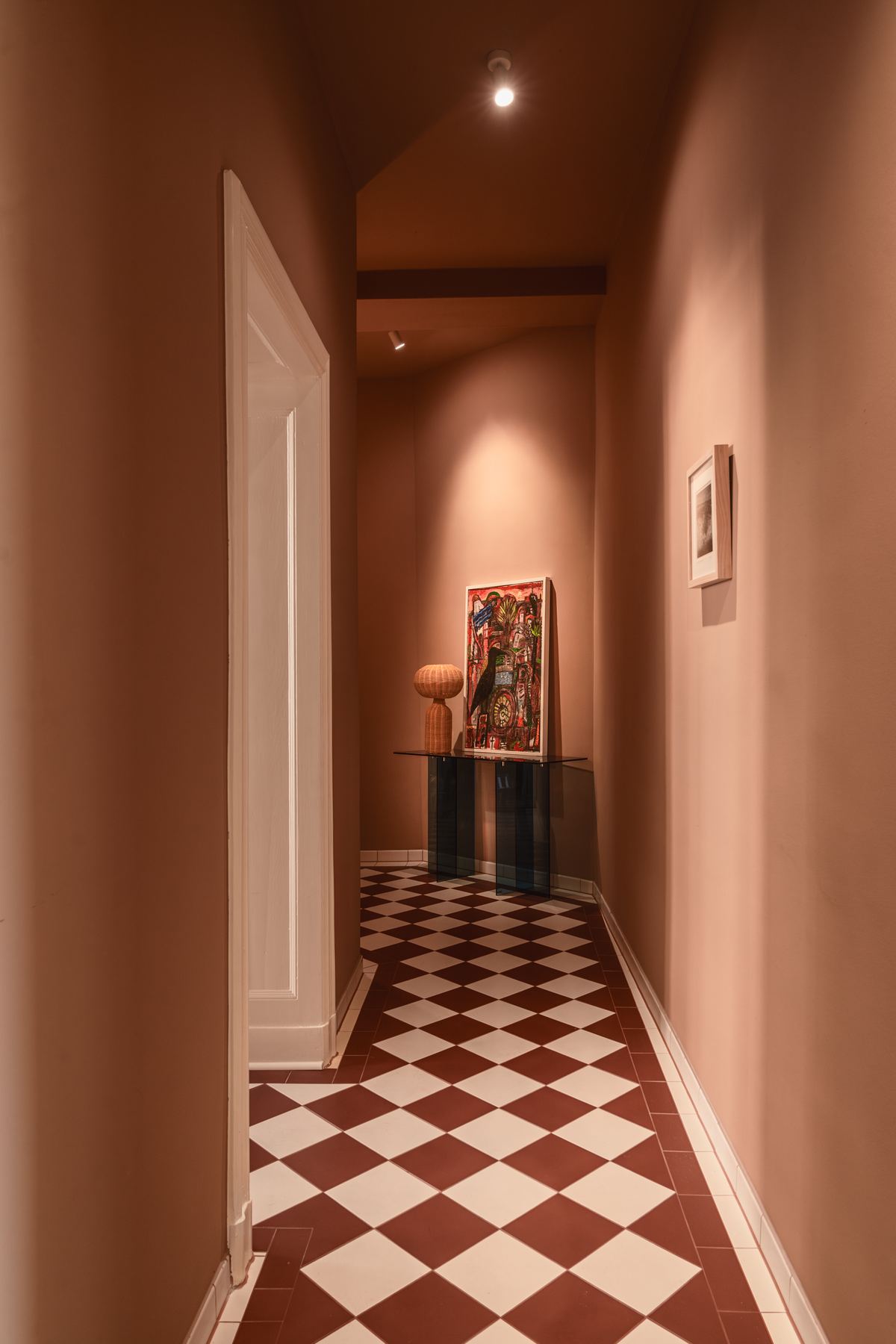 The entry hall painted terracotta, with a red and white checkerboard tile floor running toward a small console table.