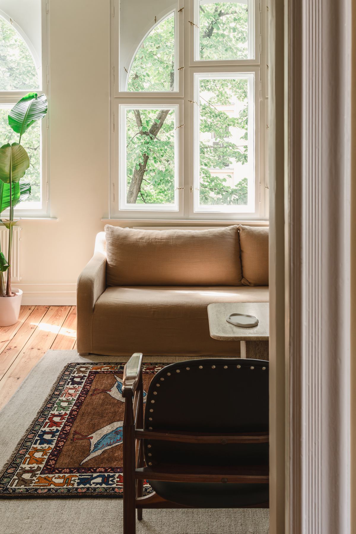 The living room seen through a doorway, with the sofa under the arched windows and trees filling the glass.