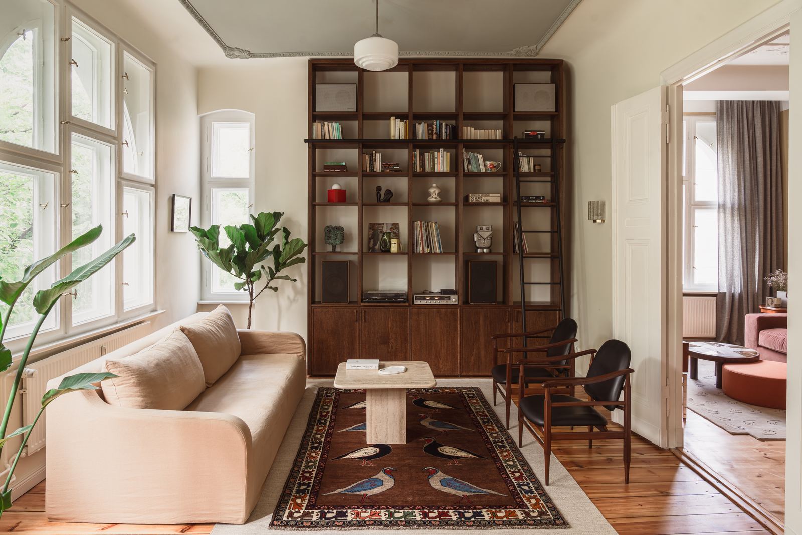 A wall of dark wood bookshelves with a sliding ladder, a record player on the lower shelf, and an open door through to the study.